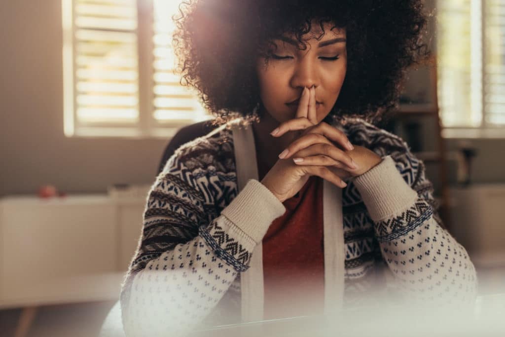 Woman in a cozy sweater sits at a table and practices mindfulness.